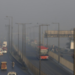 A smog-covered cityscape of Lahore with vehicles emitting smoke.