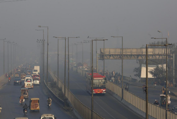 A smog-covered cityscape of Lahore with vehicles emitting smoke.